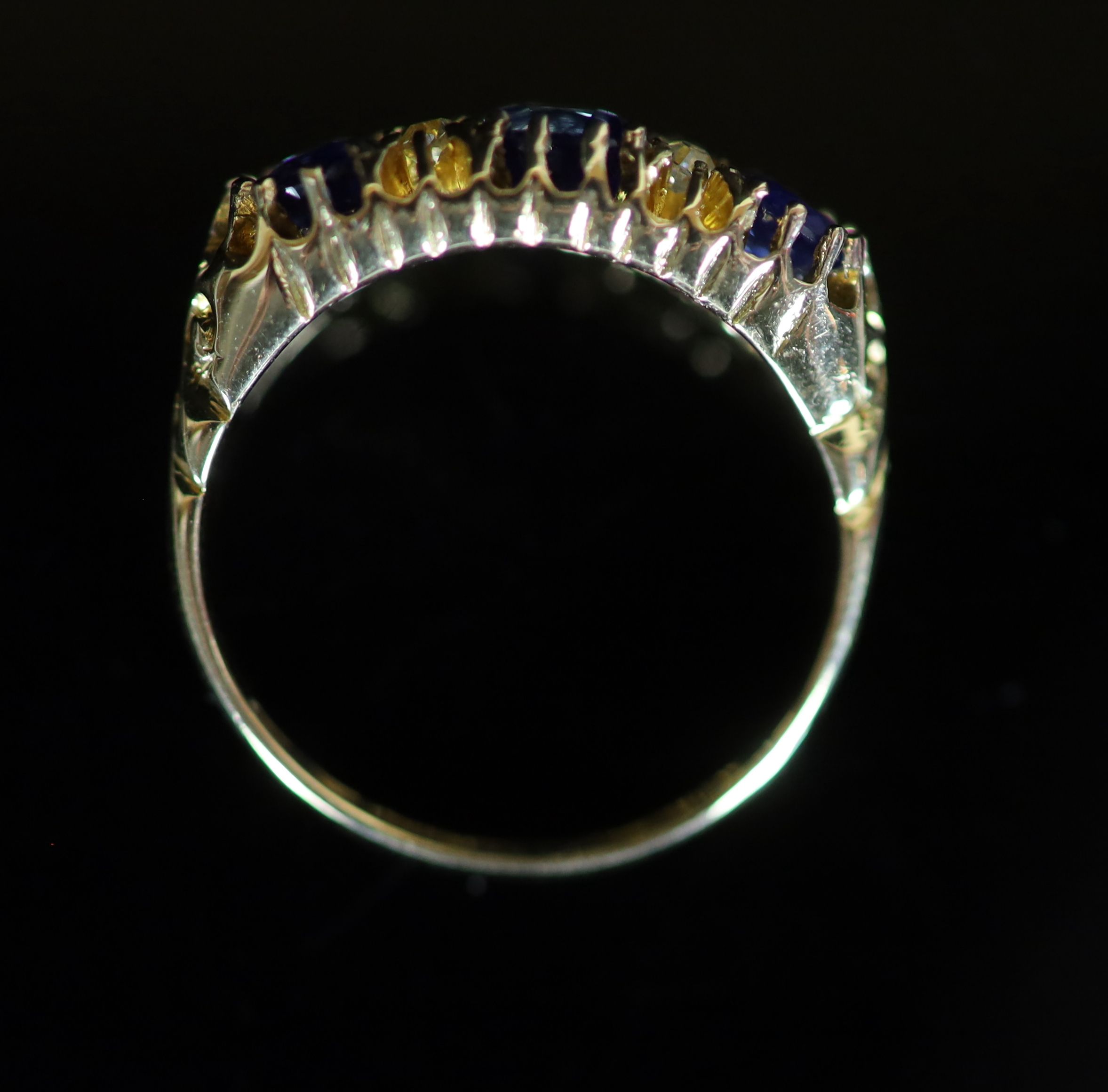 An Edwardian 18ct gold and three stone sapphire set half hoop ring with diamond chip spacers